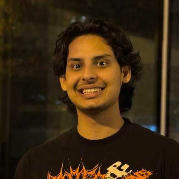 A smiling young man with brown skin and dark hair is pictured in an indoor setting