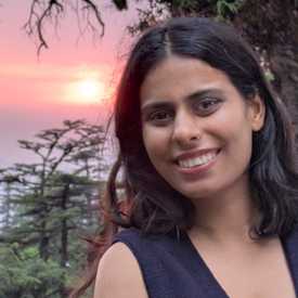A young woman with light brown skin and dark hair appears outdoors during a sunset.