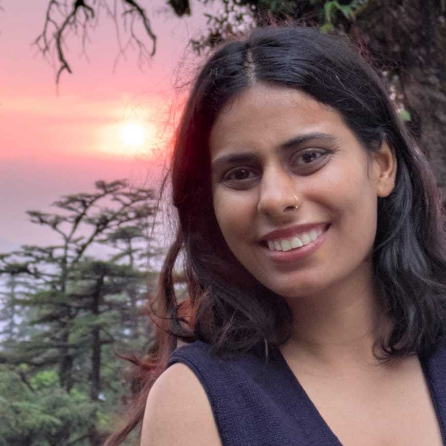 A young woman with light brown skin and dark hair appears outdoors during a sunset.