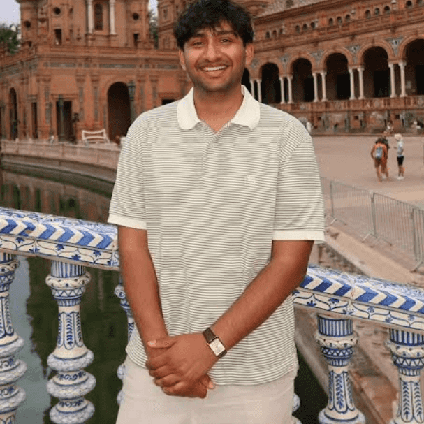 A young man standing and smiling on a bridge next to an ornate building