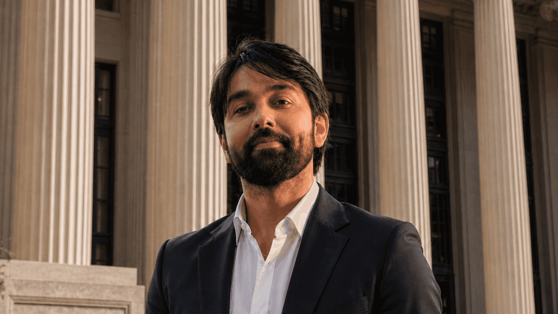 a photo of a man wearing a white shirt and dark suit in front of columns
