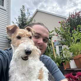 A young man appears outside a house, holding a dog 