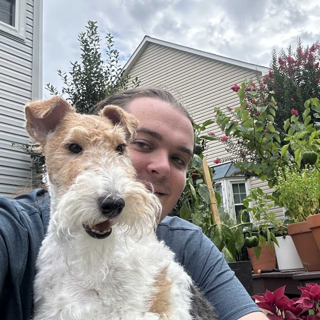 A young man appears outside a house, holding a dog 